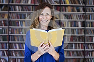 Portrait of woman over 25 in a library reading an opened book, concentrated and smart. Young college student in co-working