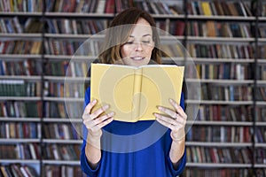 Portrait of woman over 25 in a library reading an opened book, concentrated and smart. Young college student in co-working, concep