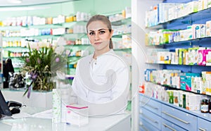 Portrait of woman pharmacist who is standing on her work place near cashbox in apothecary.