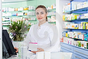 Portrait of woman pharmacist who is standing on her work place near cashbox in apothecary.