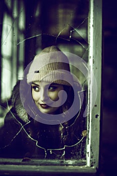 Portrait of a woman photographed through broken glass of a window.Urban exploration concept.
