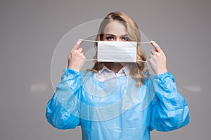 Portrait of woman in protective uniform putting on safety medical mask on face