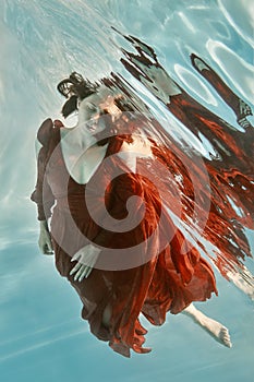 Portrait of a woman in a red dress floating underwater