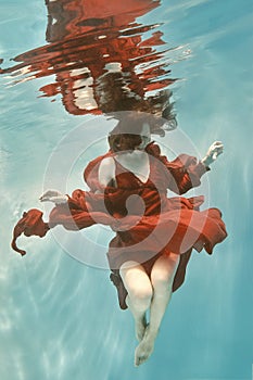 Portrait of a woman in a red dress floating underwater