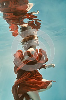 Portrait of a woman in a red dress floating underwater