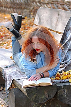 Woman in the autumn park. lying on a bench with a veil and reading a book. Autumn background