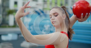 Portrait of woman in red sports costume performing callisthenics exercises with gymnastic ball outdoors, sports in the