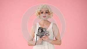 Portrait of woman with retro video camera in hands close up. Woman looking like Marilyn Monroe in studio on pink