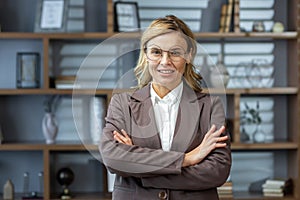 Portrait of a woman senior, director, boss, founder of the company in glasses and a brown business suit. She is standing
