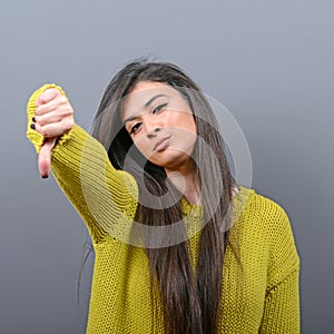 Portrait of a woman showing thumb down as disapproval against gray background