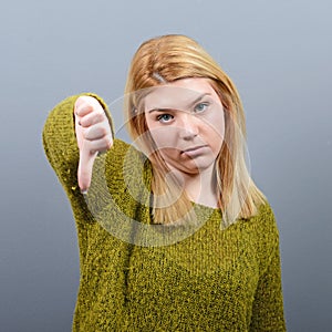 Portrait of a woman showing thumb down as disapproval against gray background