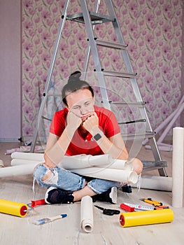 Portrait of a woman sitting on the floor with rolls of Wallpaper in his hands. Tired woman Wallpaper glue.