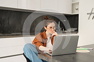 Portrait of woman sitting at home with laptop. Businesswoman managing her own business remotely from her kitchen