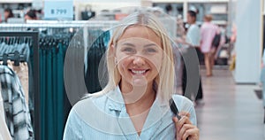 Portrait of woman smiling in clothing store looking at camera. Female happy young shopper enjoys process of shopping