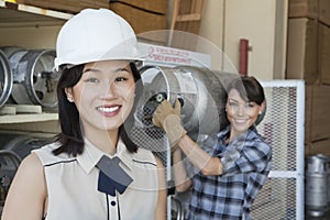 Portrait of woman smiling with female industrial worker carrying propane cylinder in background