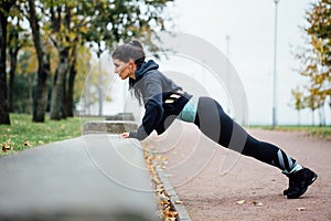 Portrait of woman in sportswear, doing fitness push-ups exercise at fall park, outdoor.