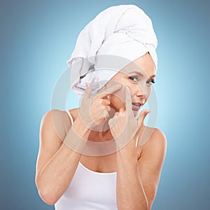 Portrait, woman and squeeze face for pimple in studio, blue background and hands press acne scar. Female model check