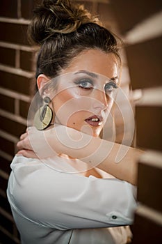 Portrait of a woman standing by the brick arch wall wearing golden earrings with tied up hair