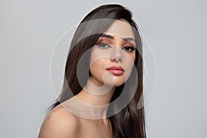 Portrait of a woman with straight dark hair and makeup on a gray background