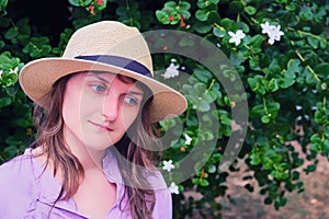 Portrait of a woman the straw hat against a tree blooming white, copy space. Girl`s face close up and little flowers in the summe