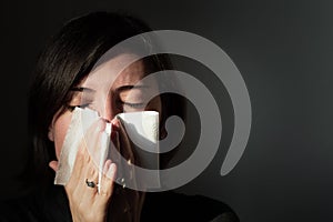 Portrait of a woman suffering from cold blowing her nose in a handkerchief