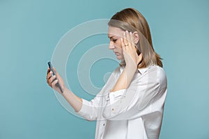 Portrait of a woman suffering from a headache looking at the information on the phone, on a blue background. Copy paste.