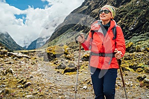 Portrait of Woman in sunglasses with backpack and trekking poles dressed red softshell jacket hiking on Makalu Barun National Park