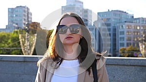 Portrait of woman in sunglasses with displeased facial expression. Serious brunette girl looks into camera at city