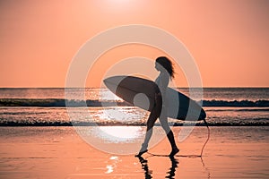 Portrait of woman surfer with beautiful body on the beach with surfboard at colorful sunset