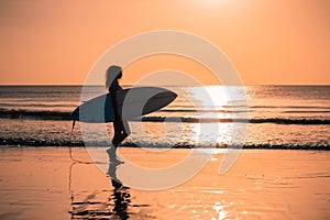 Portrait of woman surfer with beautiful body on the beach with surfboard at colorful sunset