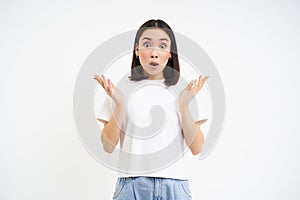 Portrait of woman with surprised face, clap hands, gasps and drops jaw with impressed face, stands over white background