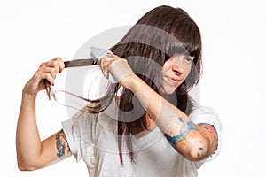 Portrait of a woman with tattoos combs a lock of hair, experiencing pain and pulling out her hair. White background. The concept