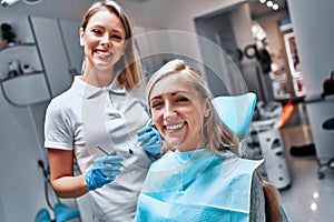 Portrait of a woman with toothy smile sitting at the dental chair with doctor on the background at the dental office
