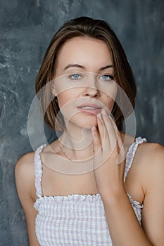 Portrait of woman in trendy white summer sarafan sexy touching lips on gray wall background closeup, free copy space