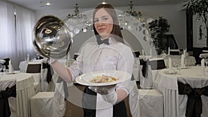 Portrait of a woman waiter holding a tray with a covered dish in a restaurant.