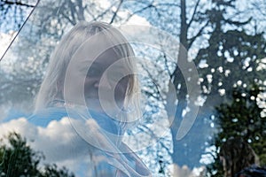 Retrato una mujer en el parque través de reflexión en vaso cual refleja árboles nubes 