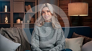 Portrait woman in warm winter sweater relaxing sitting on couch at cosiness evening home interior