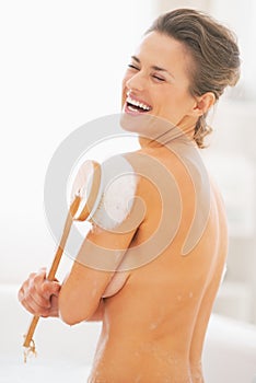 Portrait of woman washing with body brush in bathtub