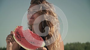 Portrait of woman with waving hair eating watermelon outdoors Girl enjoys her rest and smiles