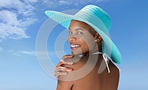 Portrait of a woman wearing a blue sun hat on the hot summer beach, enjoying a holiday by the sea. Seen from behind, with her hand