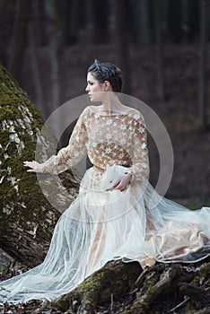 Portrait of woman wearing elegant dress sitting in a coniferous forest with rabbit in hands.