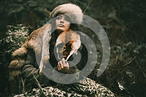 Portrait of a woman wearing fur hat and fox fur pelt on her shoulders.Shot in forest surroundings.