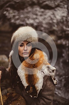 Portrait of a woman wearing fur hat and fox fur pelt on her shoulders.Shot in forest surroundings.