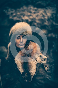 Portrait of a woman wearing fur hat and fox fur pelt on her shoulders.Shot in forest surroundings.