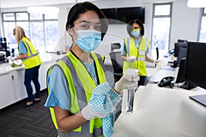 Portrait of woman wearing hi vis vest and face mask holding cleaning cloth and disinfectant