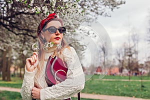Portrait of woman wearing red hair scarf and sunglasses in spring park. Retro female fashion. Headscarf and purse