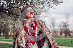 Portrait of woman wearing red scarf and sunglasses in spring park holding purse. Retro female fashion. Old money