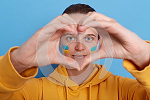 Portrait of woman wearing yellow hoodie showing love gesture with hands, making heart shape with her fingers, expressing love to