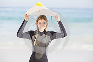 Portrait of woman in wetsuit carrying surfboard over head
