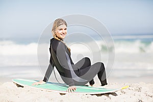 Portrait of woman in wetsuit sitting with surfboard on the beach